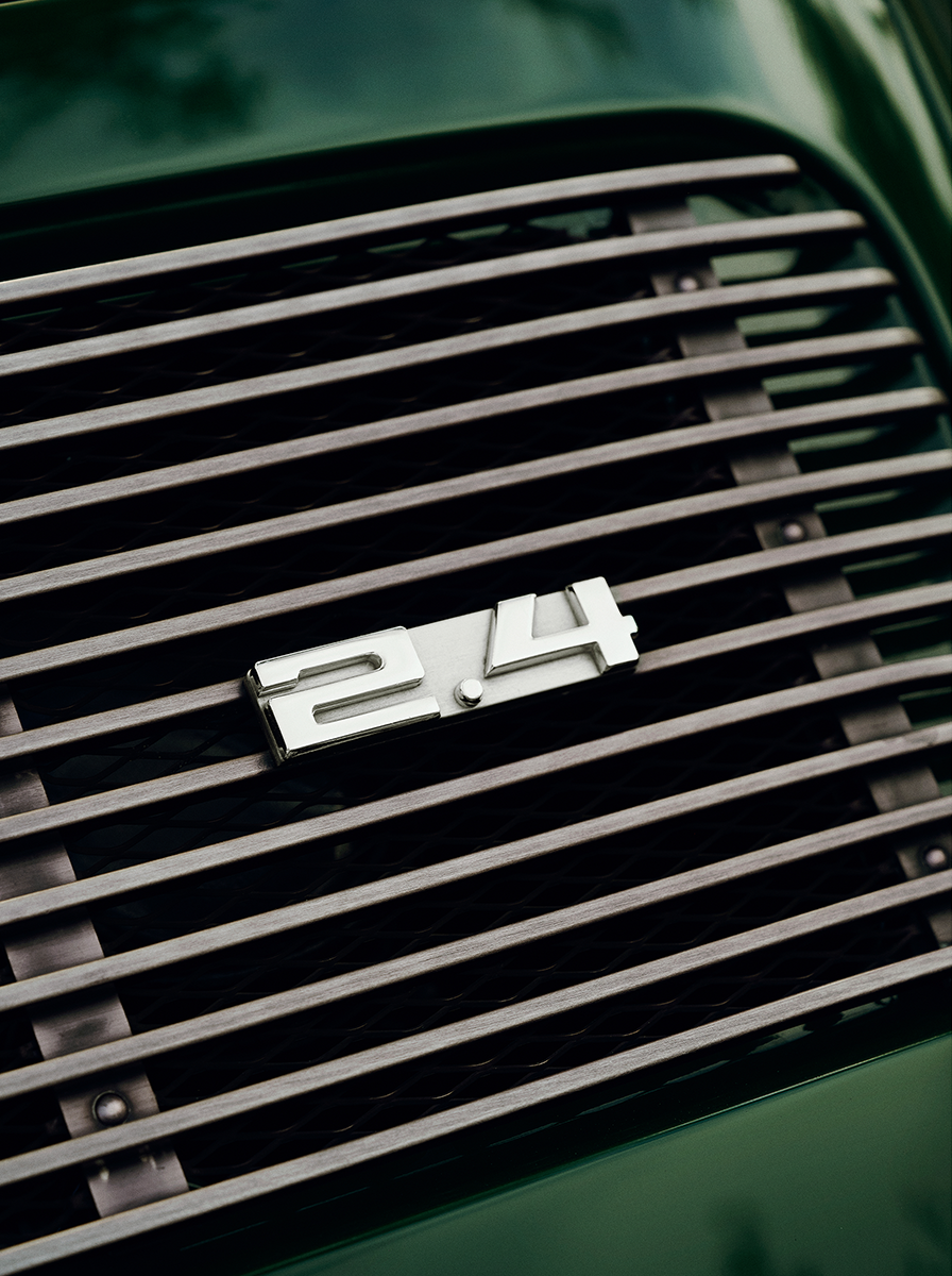 Chrome 2.4 emblem on the brushed-metal grille of a British racing green vintage sports car — close-up automotive fine art print